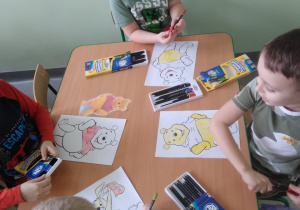 Dzieci przy stolikach kolorują bohaterów bajki "Kubuś Puchatek"
